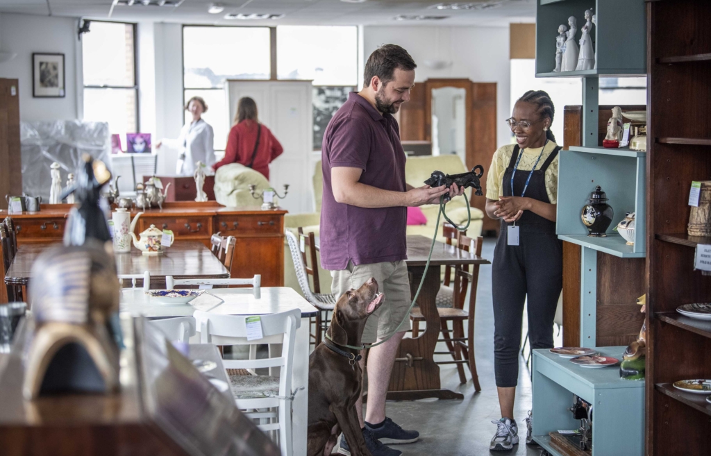 Companion Bunmi serving a customer with his dog upstairs in the Emmaus Bristol stokes croft charity shop